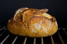 Een rond zuurdesembrood met een opengebarsten korst, afkoelend op een ovenrooster.